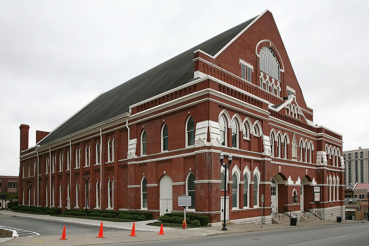 A red brick building with arched windows and white decorative trim, with orange cones in front.